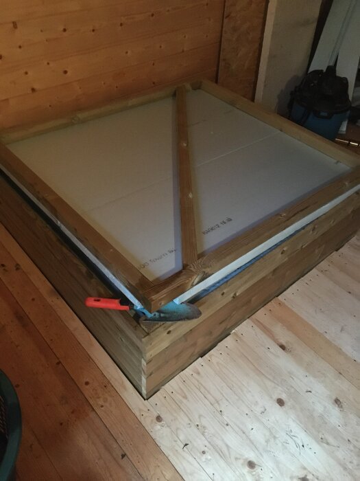 Isolerad låda med trälock och verktyg i friggebod för poolpump.