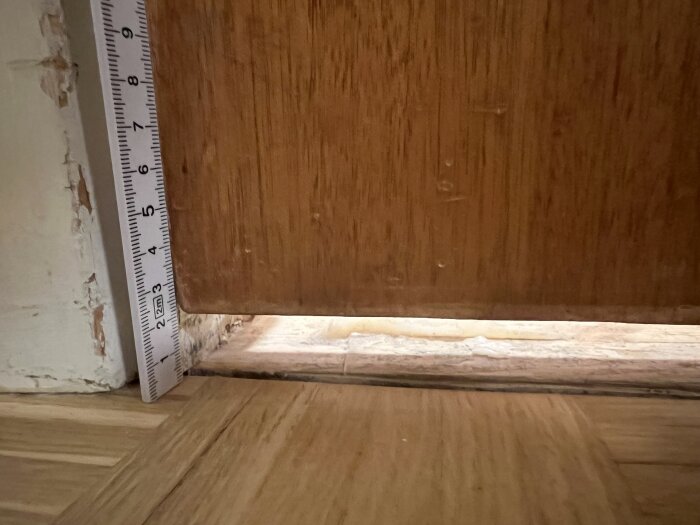 Närbild av en tröskel med en linjal som visar nivåskillnaden mellan två golv, skillnaden uppgår till cirka 1 cm.