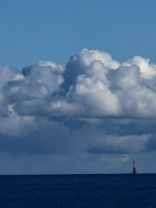 Hav med molnig himmel; en oljerigg syns vid horisonten.