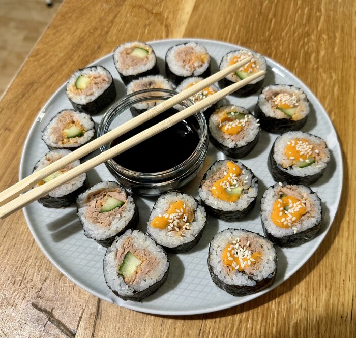 Tallerken med snabbsushi: bitar med tonfisk, gurka och sesamfrön. Sojasås i skål med pinnar ovanpå.