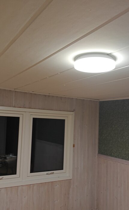 Tak med vit panel och rund taklampa, väggar av träpanel och tapet. Bild från renovering av 70-talsstuga.