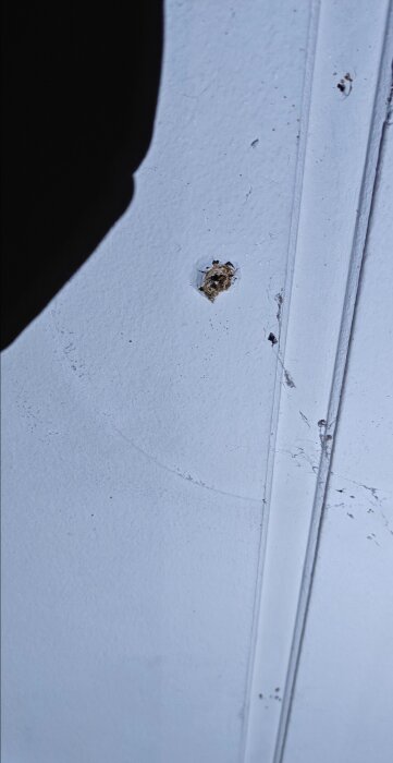 Hål i vitt tak med ojämn kant, uppkommet efter att en lampa tagits ner, omgivet av några skräp och repor på ytan.