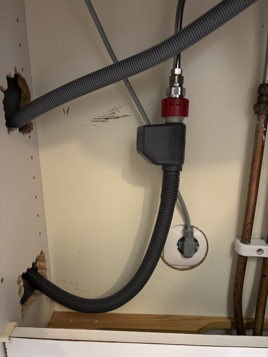 Grå vattenslang med Aquastop under diskbänk. Slangen har en böj innan den går genom ett borrat hål.