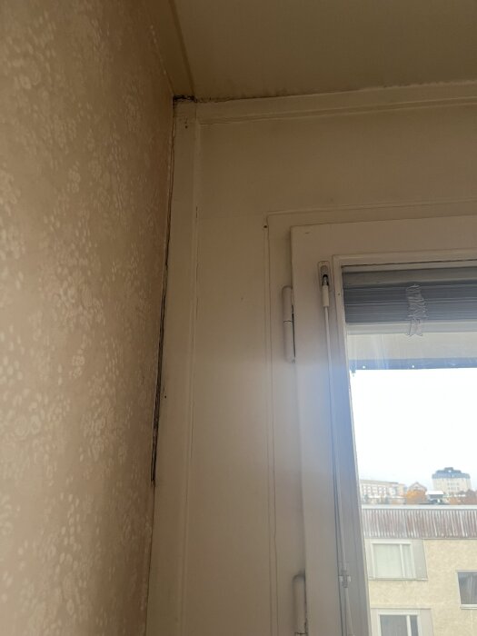 Vägg och fönsterkarm med synliga sprickor och dålig tätning, delvis bortdragen tapet, i ett kök som ska renoveras.