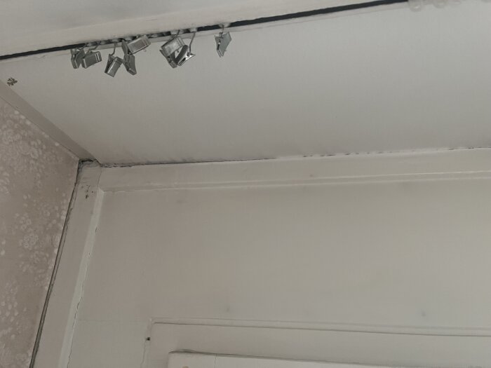 Vägg och fönster i kök med dålig tätning och avskavd tapet nära fönstret, visar områden som behöver reparation för bättre isolering.