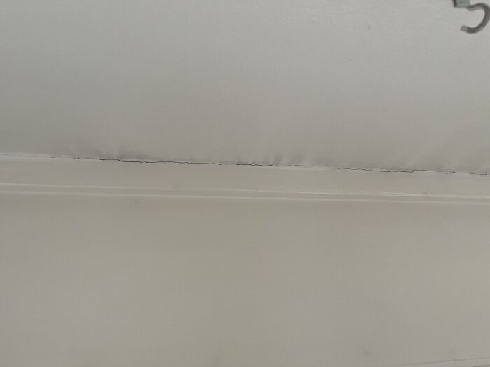 Dåligt tätad springa ovanför ett fönster i köket med sprickor i färg och tapet.