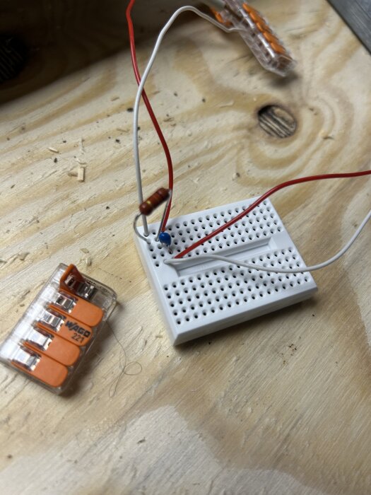 Mini-breadboard med kablar och komponent, inklusive en resistor och kopplingsklämma, på träbord.