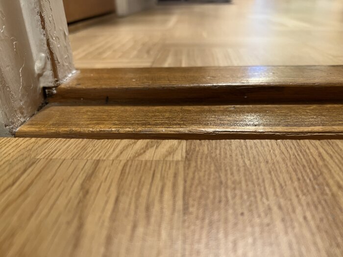 Glipa mellan parkettgolv och gammal tröskel i lägenhet, fokus på det estetiska och möjliga lösningar för att fylla gapet.