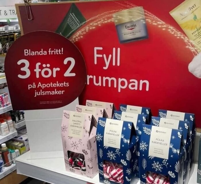 Förpackningar med polkagrisar och hallon & lakrits karameller på en hylla, skylt med "3 för 2 på Apotekets julsmaker".