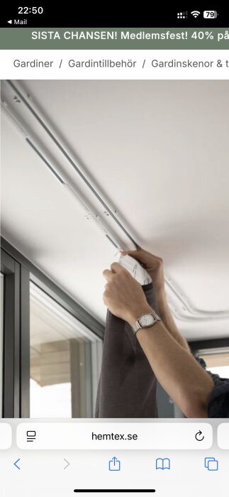 Person hänger upp gardin på ett par U-skenor i taket nära ett fönster. Gardinskenorna är silverfärgade.