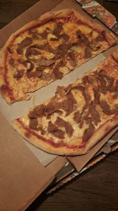 Pizza med köttbitar i en kartong, med två stora skivor synliga.