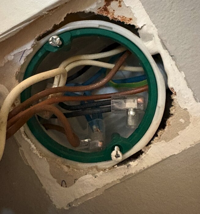 Eluttagets insida med flera exponerade kablar i olika färger, monterade i ett runt väggdosa med grön ram.