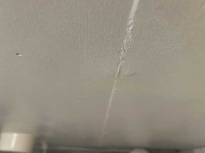 Innetak i tvättstuga med slät yta, synliga skarvar och utbuktningar från spik, grå och stenhård yta; möjligtvis fibercementskiva.