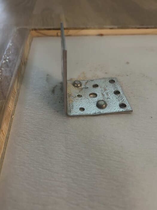 Vinkeljärn fastbultat i golvskiva av trä, synlig bult och omgivande området.
