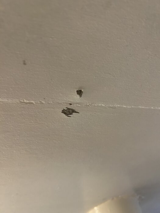 Hål i vägg där borrningen påträffade grått, hårt material under ytan, ingen spik synlig.