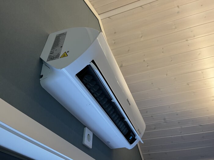 Samsung luftvärmepump monterad på väggen i ett rum med trätak.