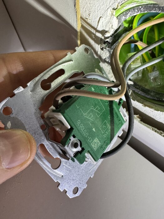 NEXA MCMR-2000 strömbrytare med inkopplade kablar i olika färger, hålls av hand nära en väggdosa med synliga kablar.