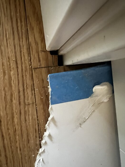 Glipa mellan nylagt parkettgolv och dörrkarm, med synlig sockelbit och ojämn kantfärg som framhäver problemet.