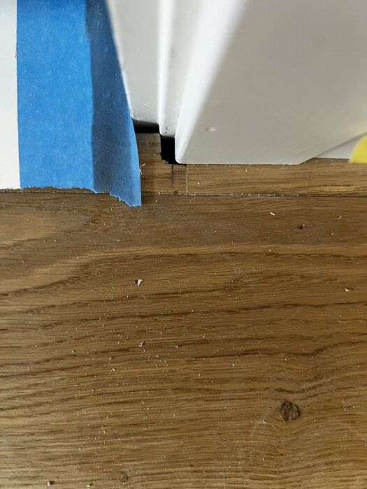 Glipa mellan nylagt parkettgolv och dörrkarm med blå tejp på väggen, synlig i vardagsrum.