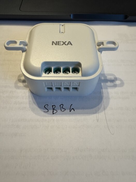 Nexa trådlös mottagare med anslutningsportar synlig ovanpå ett papper med text.