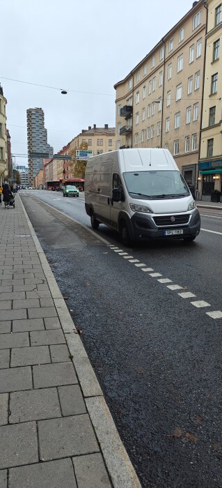 Skåpbil parkerad vid vägkanten på en stadsgata med byggnader i bakgrunden.
