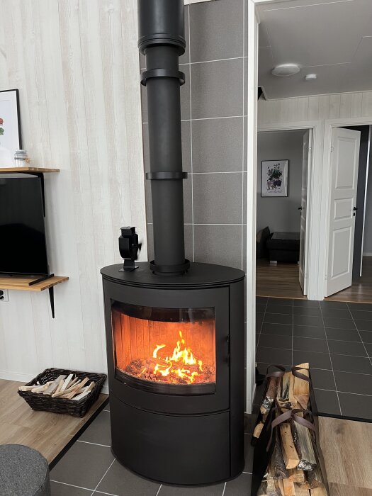 Svart kamin i rum med eld inuti, omgiven av ved på golvet.