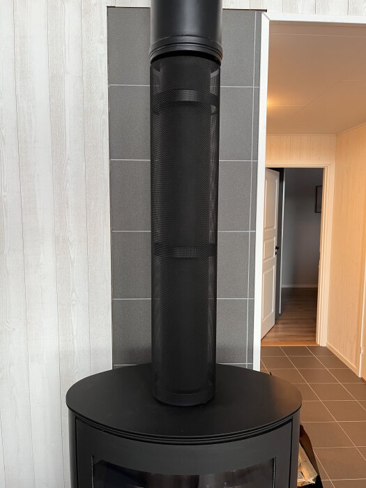 Kamin med oisolerat rökrör och finmaskigt galler av sträckmetall för ökad värmeeffektivitet i en stuga.
