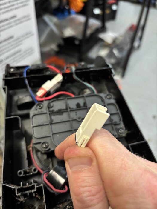 En person håller i ett vitt kontaktdon märkt med "AMP" framför en öppnad elektronikenhet med synliga sladdar.