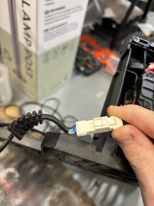 En hand håller i en vit AMP-kontaktdon ansluten till en svart kabel på en arbetsyta.