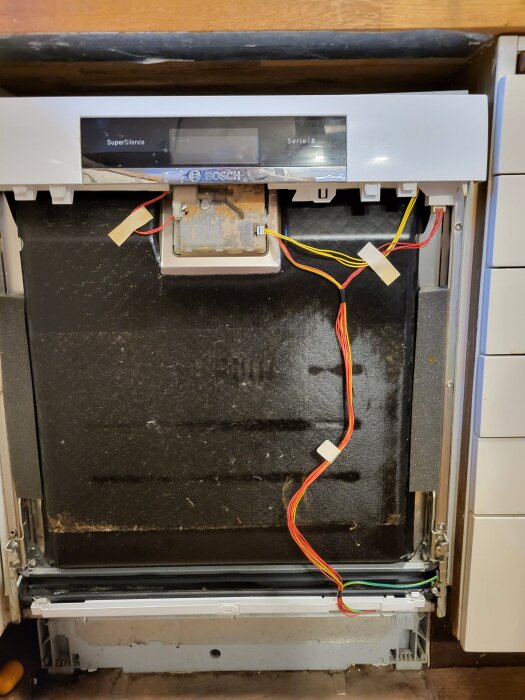 Öppnad diskmaskin med borttagen frontpanel, exponerad elektronik och kablar samt en lös metallskena, Bosch SuperSilence Serie 8.