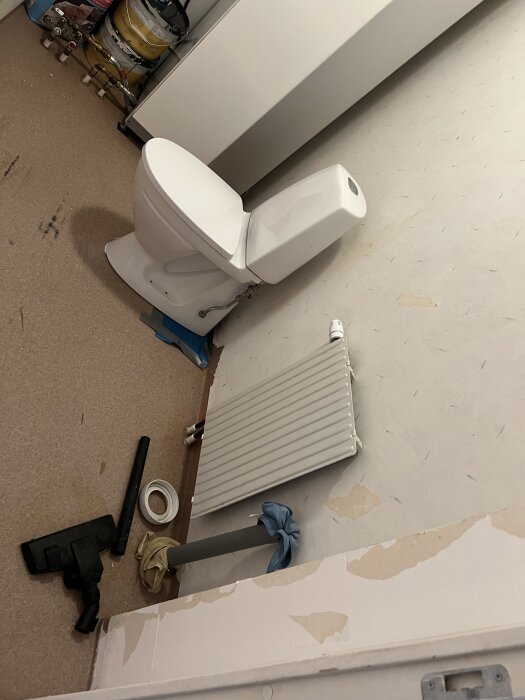 Rum med toilett, radiator, och lite byggmaterial i ett pågående projekt för att installera en gästtoalett.