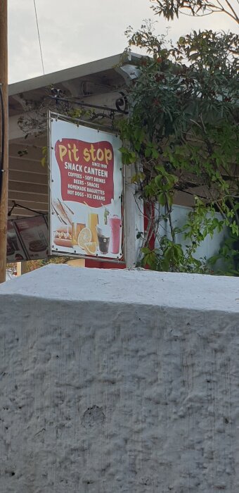 Skylt för "Pit Stop" snackkantin, erbjudande om kaffe, drycker, öl, snacks, baguetter, korv med bröd och glass.