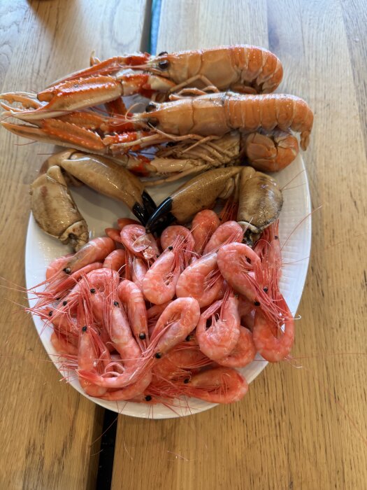 Skaldjur på en tallrik, med kräftor och räkor upplagda snyggt på ett träbord.