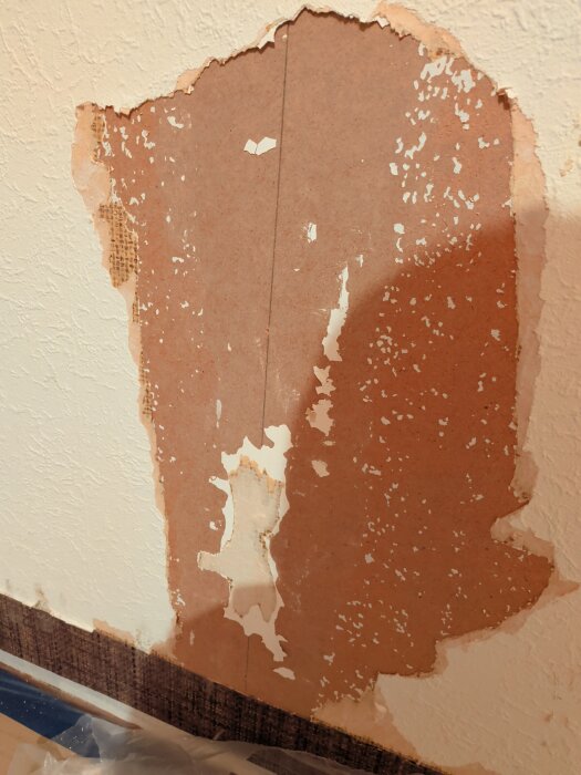 Väggen visar borttagen strukturtapet med exponerat brunt underlag och vita rester, potentiellt lim eller spackel, på ett hus byggt 1976.