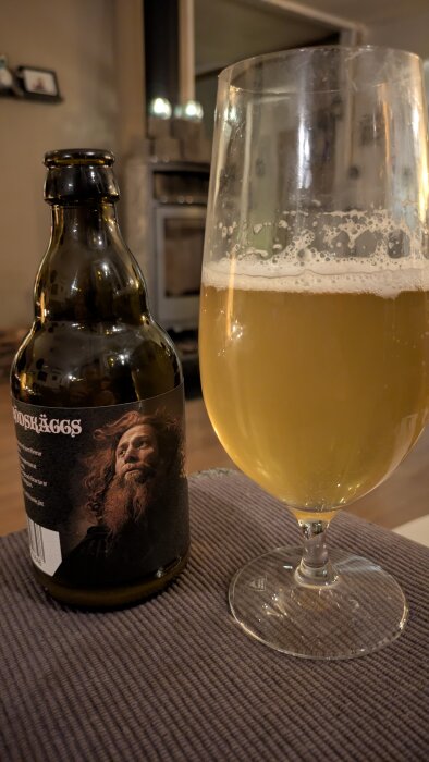 Flaska och glas med öl på ett bord, bakgrund av ett hemtrevligt rum.
