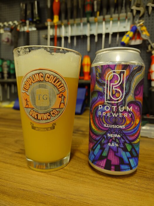 Ett glas med skummande öl och en färgglad burk från Potum Brewery, etiketterad "Illusions NEIPA 6.5%", på ett bord i verkstadsmiljö.