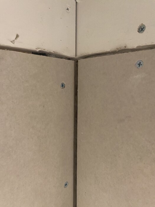 Närbild av gipsskivor monterade i ett hörn med synliga skruvar och en springa mellan skivorna.