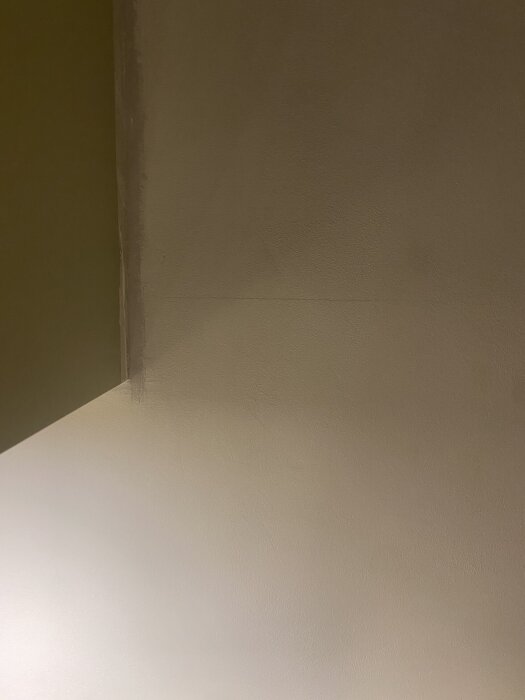 Mörk bild av en vägg med synlig spricka och ojämn yta efter spackling, med en skarv rakt över i mitten av bilden.