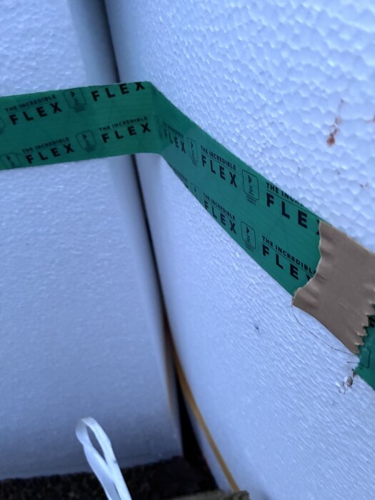 Grönt flextejp applicerat på vit isolering runt en terrasspool, synlig glipa mellan tekniklåda och poolens isolering.