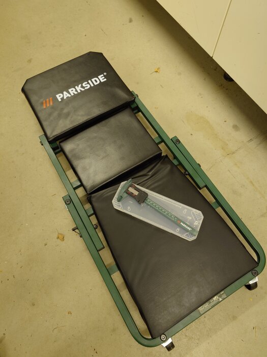 Montagebräda "Parkside" och skjutmått i plastförpackning ligger på garagegolvet.