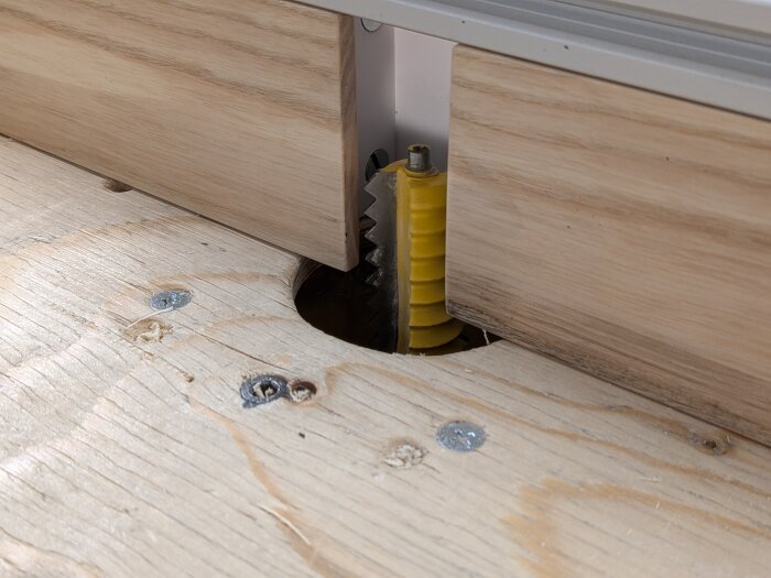 Anhållet på fräsbordet med justerbara träbitar och en gul del av en fräsklinga synlig genom en öppning.