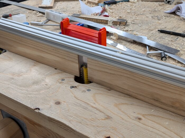 Fräsbord med nyjusterat anhåll av aluminium och trä, omgivet av verktyg och sågspån på arbetsbänk.