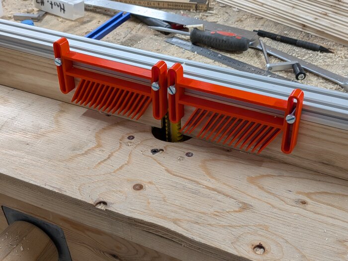 Anhåll till fräsbord med justerbara röda plastdetaljer, monterat på träskiva, med verktyg och material i bakgrunden.