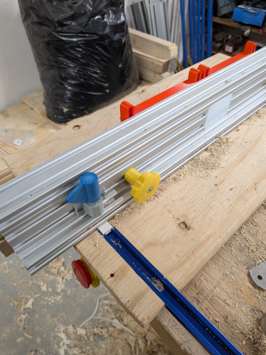 Fräsbord med justerbart anhåll av aluminium och trä, komplett med färgade 3D-utskrifter och snickeridetaljer, liggandes på arbetsbänk.