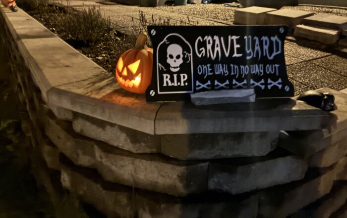Gravsten i Halloween-stil med "Grave Yard" och en lysande pumpa med ansikte på en mur.