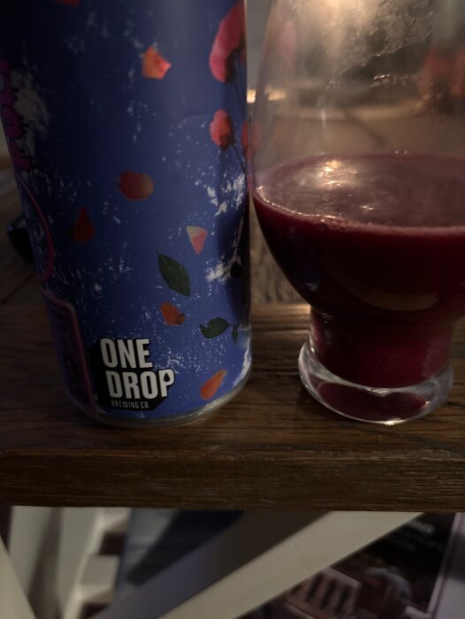 Blå burk från One Drop Brewing och ett glas med tjock, mörkröd dryck på ett träbord.