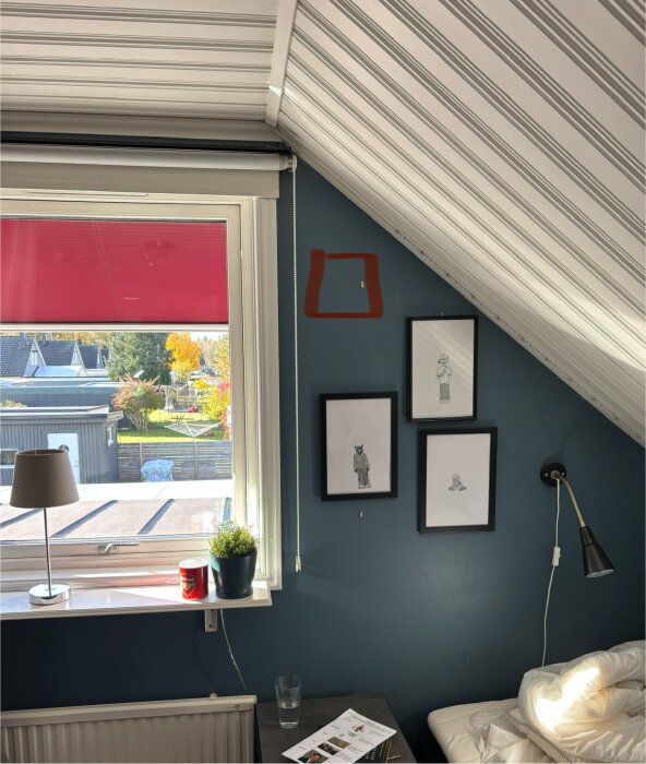 Ett hörn av ett sovrum med blå väggar, tre tavlor, en skrivbordslampa och ett fönster, markerad plats för ventilinstallation.