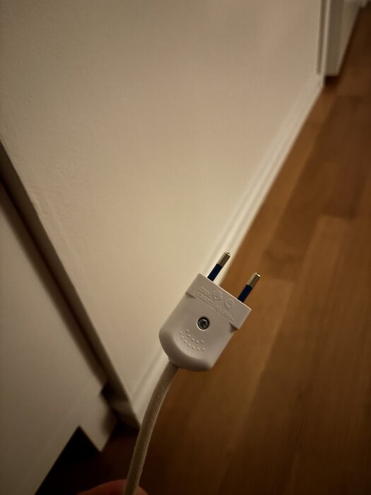 Vit, ojordad stickkontakt med två metallstift, hålls i en hand mot en ljus vägg.