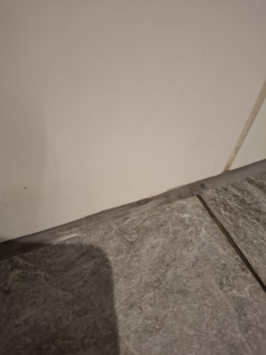 Vitt väggkakel med brunt fog och grått klinkergolv med skugga. Möjligtvis fokus på fogens tillstånd mellan kakel och klinker.