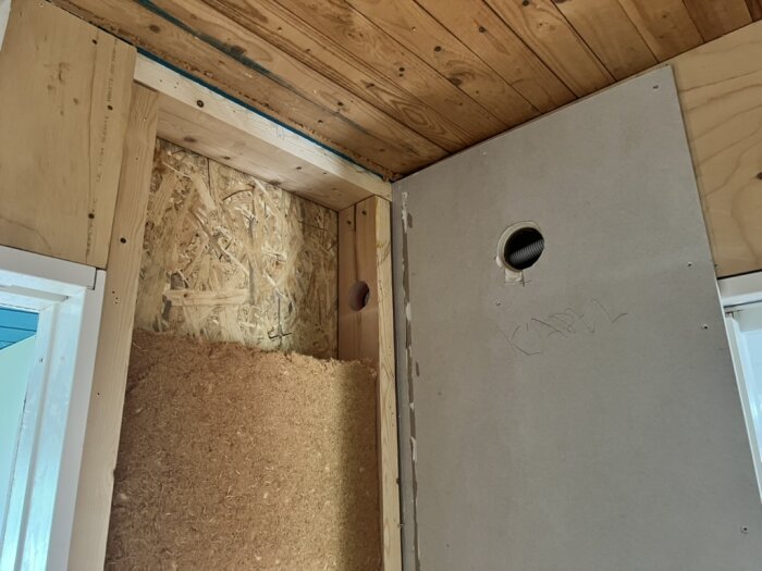 Inre vägg med hål för högtalarkabel. Träpanel i taket och OSB-skiva ovanför isolering syns. Hölje för kabel dragen genom ett hål.
